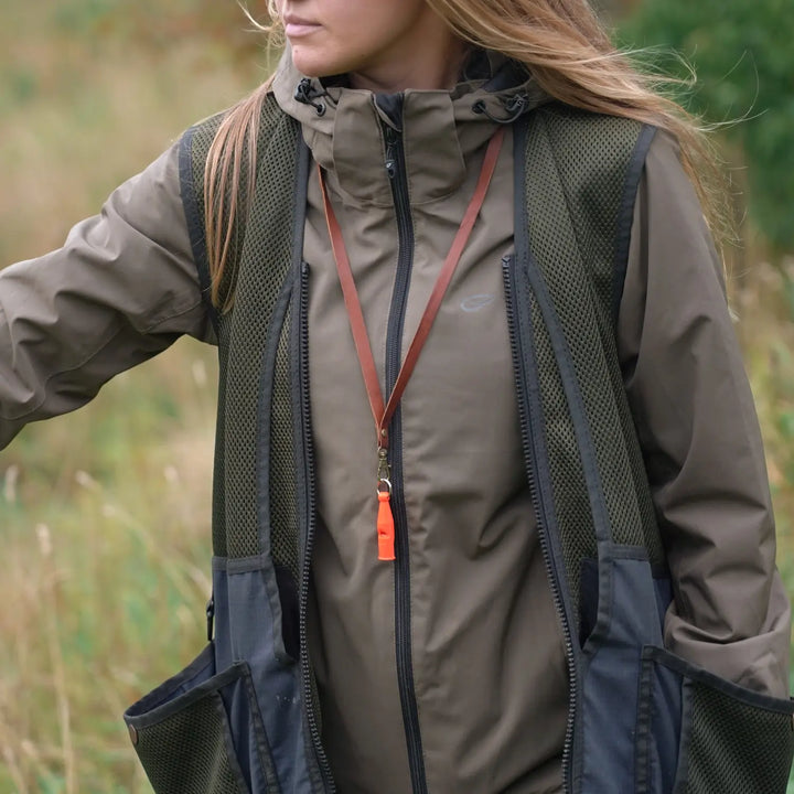 Miljöbild tjej på fält med acme pro trialler 212 neon orange med junies visselpipsband läder cognac #color_neon-orange