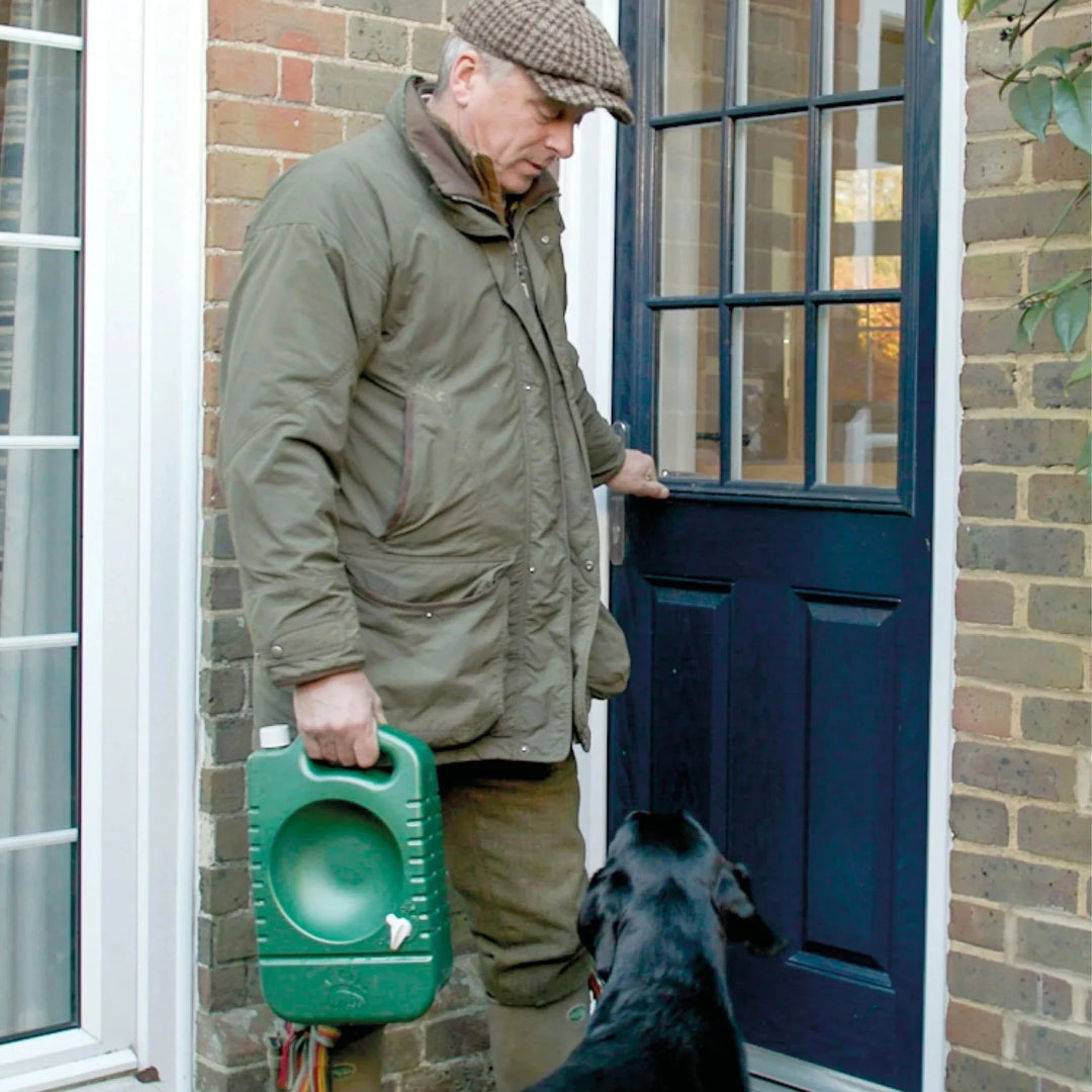 man i jaktkläder bär på portabel hundvattenskål från porta-bowl bredvid sin svara labrador hund