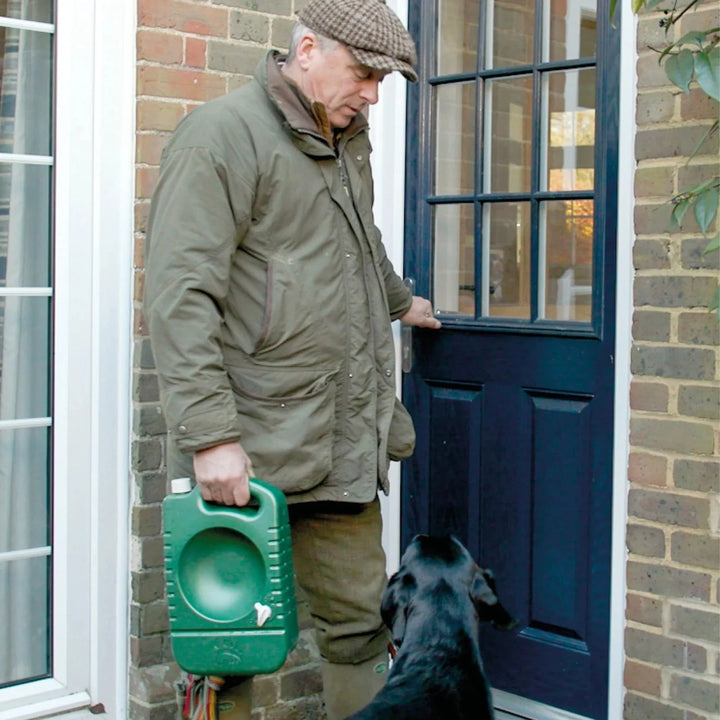 man i jaktkläder bär på portabel hundvattenskål från porta-bowl bredvid sin svara labrador hund